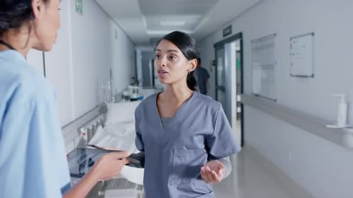Diverse doctor and nurse using tablets and talking in corridor at hospital, in slow motion