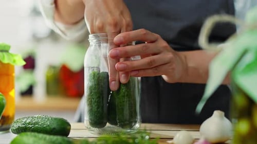 Garlic, active woman Stacks preparing cucumbers in a glass jar for preservation in the kitchen home