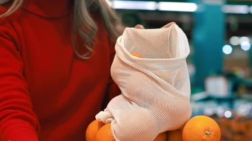 Mujer recogiendo naranjas en una bolsa reutilizable en una tienda. Temáticas del Día de la Tierra y la Ecología