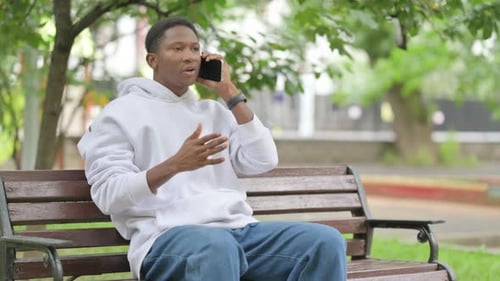 Casual African American Man Talking on a Smartphone while Sitting Outdoor