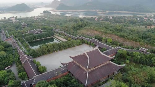 Drone aerial view in Vietnam flying over a buddhist temple area filled with green trees in front of