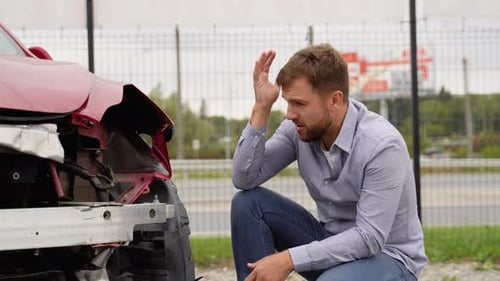 Man Kneeling by Damaged Car After Auto Accident