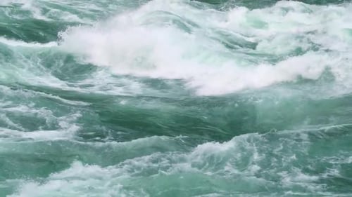 Mächtige, tosende Stromschnellen mit weißem Schaum und Sprühnebel in einer schnell fließenden Flusslandschaft.