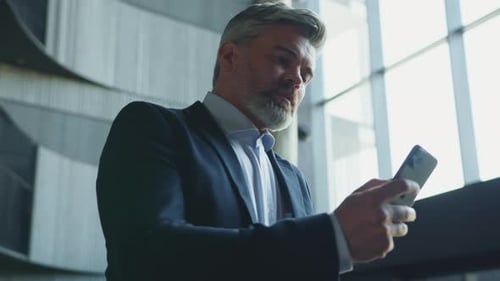 Footage of Confident Focused Middleaged Man Holding Mobile Phone in Hands Texting and Looking Away