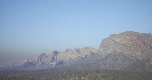 Majestic Mountain Range Under Clear Blue Sky with Evergreen Forest Below