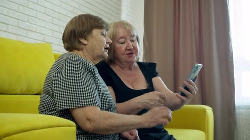 Senior Women Watching Video on Smartphone Together Indoors