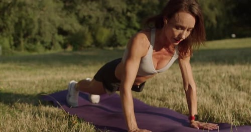 Woman Doing Pushups in Grassy Field on Sunny Day