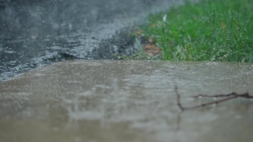 Heavy Rain Water Drops Falling Into Big Puddle on Asphalt Flooding the Street on Suburb Close Up
