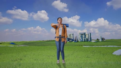 Corps entier d'une randonneuse asiatique montrant le geste des pouces vers le bas à Stonehenge