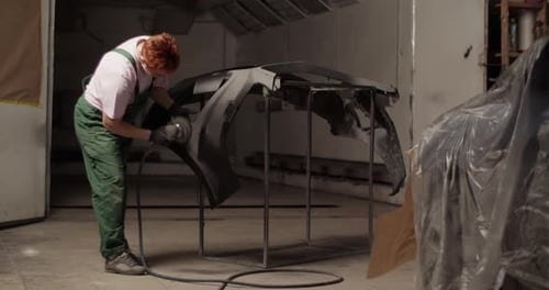 Repairwoman Sanding Bumper Near Vehicle