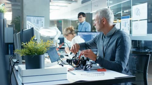 Electronics Engineer Works with Robot, Manipulating its Responses and Checking Data with Laptop Com