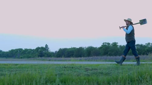 Man with Shovel Walking Across Green Field