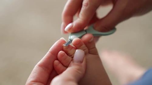 Caring about the child. Mom’s hands hold the tiny toes and cut the toenails with scissors. Close up.