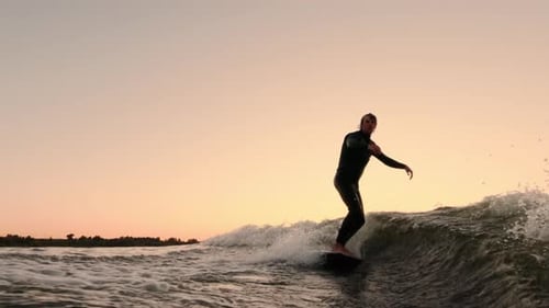 Man Wake Surfing on River Wave at Sunset