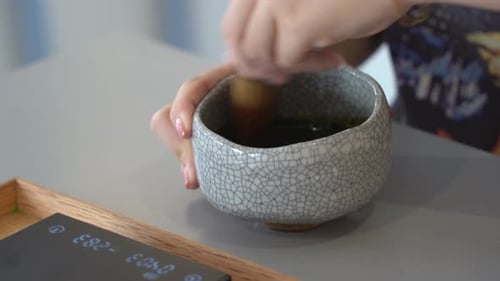 Young lady's hands whisking and mixing matcha green tea in the handmade ceramic bowl with bamboo whi