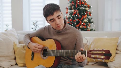 Young Man Plays Guitar at Home Christmas Time