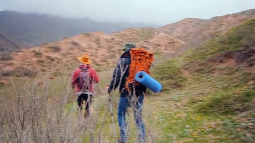 Deux randonneurs se déplaçant sur un terrain montagneux accidenté avec des sacs à dos et des bâtons de randonnée pour naviguer dans la nature