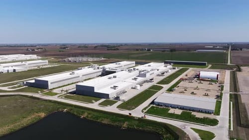 Orbiting drone shot above a large hyperscale data center campus with retention pond in foreground