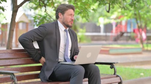 Man Outdoors on Bench Typing with Back Pain