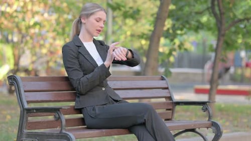Woman Using Smartwatch While Sitting on Park Bench