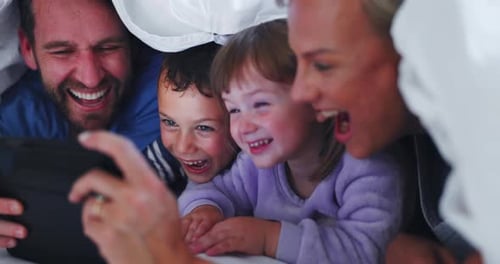 Family Laughing Together While Watching Tablet Under Sheets