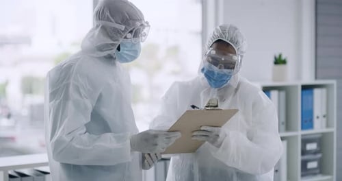 Two Healthcare Workers in Protective Suits Discussing Notes