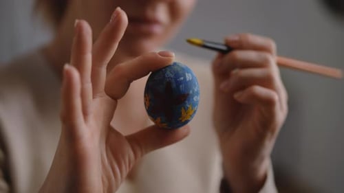 Closeup A Woman Holds an Easter Egg in Her Hand and Touches Up the Ornament on It with a Paintbrush