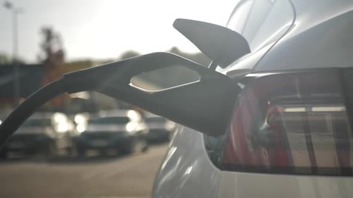 Rear View of an Electric Car Being Charged at a Charging Station Using a Cable Plugged Into an