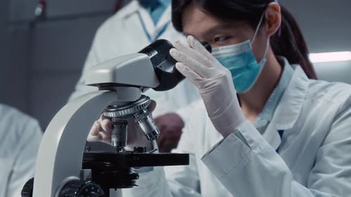 Chinesische Studentin analysiert Probe im Mikroskop in der Universitätspraxis