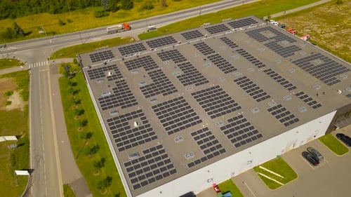 Aerial view of a rooftop with hundreds of solar panels during sunny day, highway visible in the back