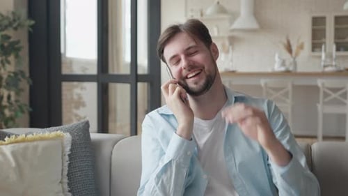 Bearded Man Smiling on Smartphone on Sofa