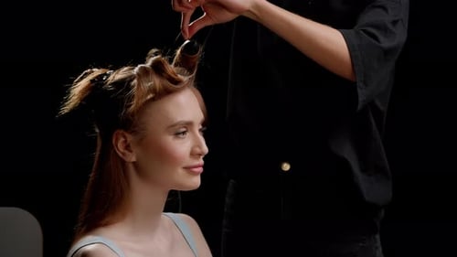 Hairdresser Using a Curling Iron on a Young Woman's Reddishbrown Hair with the Model Seated and