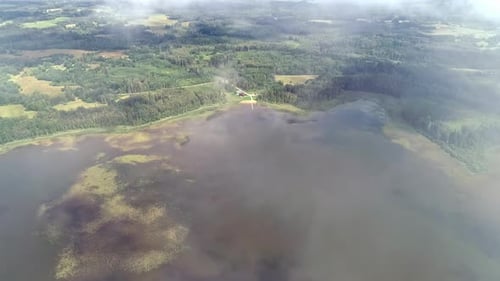 Aerial View Through Clouds Of Green Forest Landscape Around Vast Wetland With Moss.