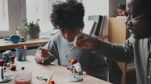 Boy and Adult Painting a Model Solar System Together