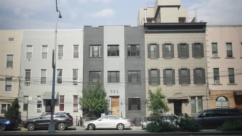 A colorful procession of cars passes before a row of multicolored Brooklyn houses, others nestled ne