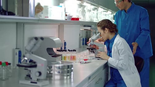 Scientist using microscope in lab, colleague walks in