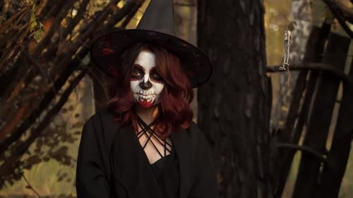 Witch with a Dead Man's Makeup in Nature Smiles and Blows a Kiss