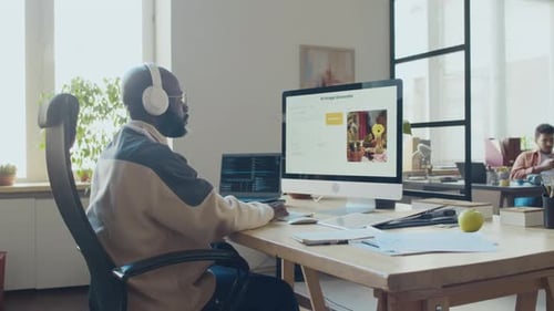 Schwarzer Mann mit Kopfhörern schreibt Code für KI-Bildgenerierungssoftware im Büro