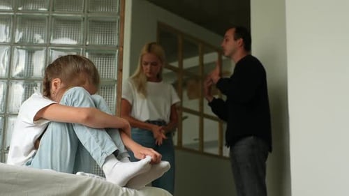 Lowangle View of Sad Little Girl Crying Suffering with Head on Knees While Parents Quarrelling and