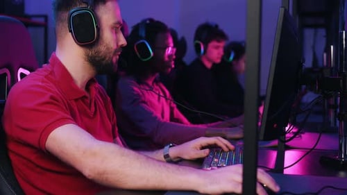 View from the side, sitting. Gamers are playing video game by computers.
