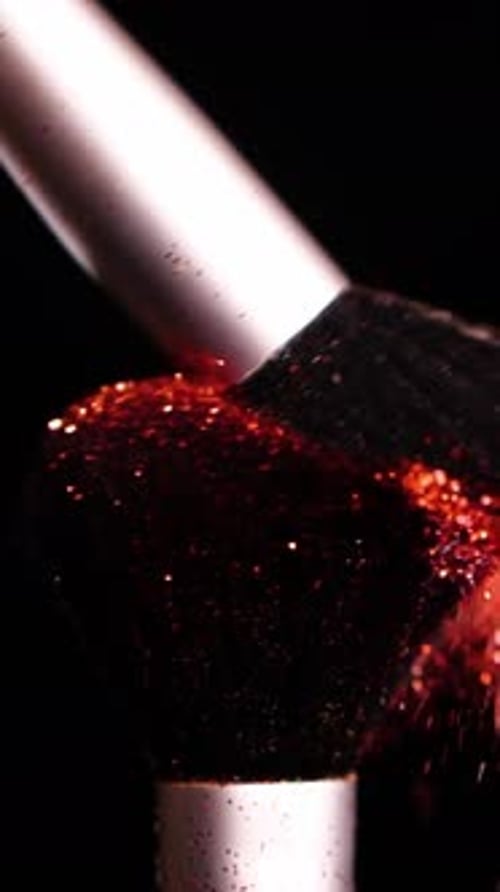 Vertical Screen Makeup Brushes Touch Each Other on Dark Background and Small Particles of Red