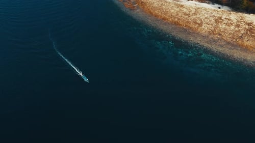 Un bateau à moteur se déplace dans la mer près de l'île, vue aérienne de haut en bas