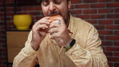 Man Enjoying Burger at Table Indoors