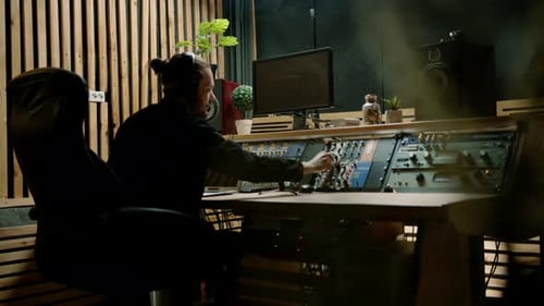 young sound engineer with headphones working in a music studio with monitors and an equalizer