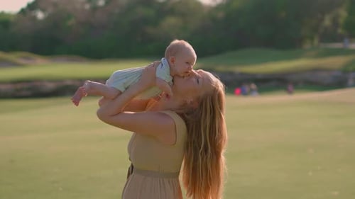 A Young Woman is Standing on a Lush Green Lawn Holding Her Newborn Baby in Her Hands Slowmotion