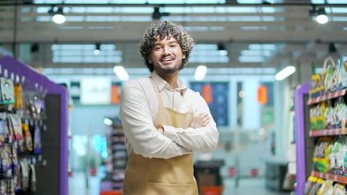 Portrait of a salesman male worker in a supermarket food market looking at camera smiling. Man