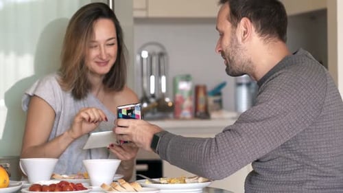 Couple eating breakfast at home, using tablet and phone