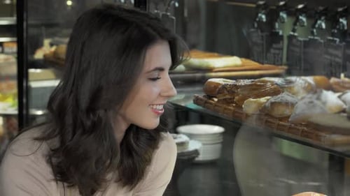 Joyful Woman Delightfully Selecting Desserts From a Tempting Bakery Display