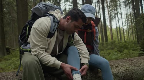 Man Examining Sprained Leg of Girlfriend during Hiking Trip in Forest