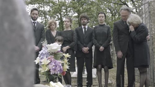 Mourners at Cemetery Gather Around Flowers in Grief